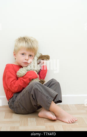 Unglückliches Kind auf dem Boden sitzend mit einem stofftier. Stockfoto