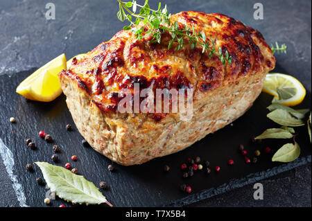 Köstliche ganze Hähnchen Hackbraten serviert auf einem Schiefer Fach mit Zitronenscheiben und frischem Thymian auf einer konkreten Tabelle, horizontale Ansicht von oben, close-up Stockfoto