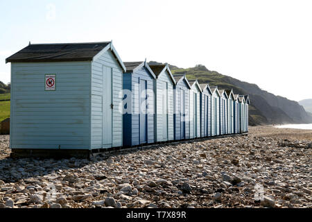 Charmouth, Dorset, Großbritannien - hölzerne Badekabinen am Kiesstrand in Charmouth mit blauen Himmel im Hintergrund Stockfoto