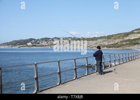 Fischer Angeln an der Küste Charmouth, Dorset an einem sonnigen Tag mit Lyme Regis in der Ferne, UK 2019 mit Kopierraum Stockfoto