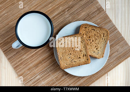 Zwei Scheiben Toast Brot und Zinn Becher Milch auf einem Holztisch, Setup Stockfoto