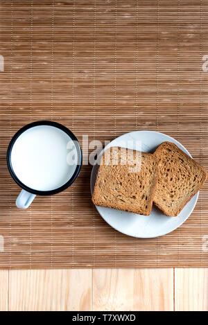 Zwei Scheiben Toast Brot und Zinn Becher Milch auf einem Holztisch, Setup Stockfoto