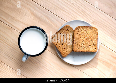 Zwei Scheiben Toast Brot und Zinn Becher Milch auf einem Holztisch, Setup Stockfoto