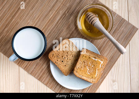Zwei Scheiben Toast mit Zinn Becher Milch und Krug Honig auf einer hölzernen Table Setup Stockfoto