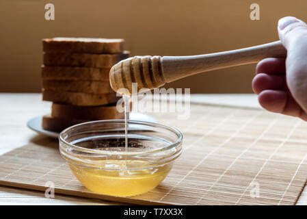 Krug Honig Honig mit Pendelarm mit Toast Brot im Hintergrund auf einem Holztisch, Setup Stockfoto