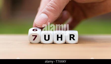 Konzept für das frühe Aufstehen am Morgen. Hand einen Würfel und ändert die Zeit von 6 Uhr (6 Uhr" in Deutscher Sprache) bis 7 Uhr (7 Uhr" in Deutsch), Stockfoto