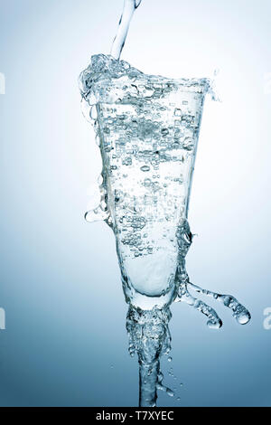 Gießen und Überfüllen des Wassers auf ein schickes Glas auf blauem Grund Stockfoto