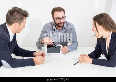 Unternehmer, die etwas auf leeren Bildschirm digital Tablet an seine Kollegen auf einer Konferenz. Stockfoto