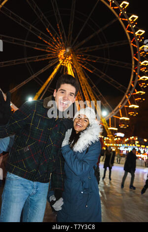Gerne fröhliche junges Paar, das Spaß am Eislaufen Park bei Nacht Stockfoto