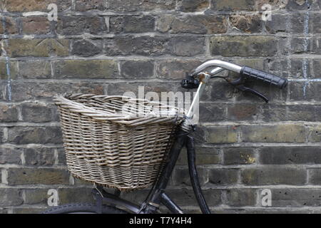 Bild von einem altmodischen Fahrrad, das hat einen Weidenkorb auf der Vorderseite aufgestützt gegen die Wand Stockfoto