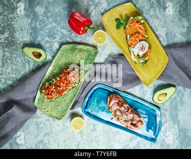 Bruscheta mit verschiedenen Füllungen auf Blau, Grün und Gelb. Schöne Gerichte. Hellgrau hinterlegt. Restaurant Menü Stockfoto