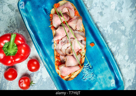 Auf einem blauen Platte des bruschet mit Rindfleisch und Tomaten, daneben ist eine rote Paprika Tomaten. Hellgrau strukturierten Hintergrund. Schöne Servieren von Speisen. Restaurant Menü Stockfoto