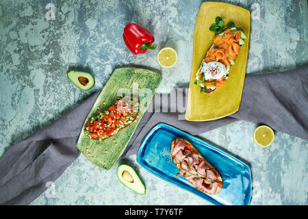 Bruscheta mit verschiedenen Füllungen auf Blau, Grün und Gelb. Schöne Gerichte. Hellgrau hinterlegt. Restaurant Menü Stockfoto