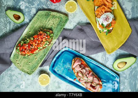 Bruscheta mit verschiedenen Füllungen auf Blau, Grün und Gelb. Schöne Gerichte. Hellgrau hinterlegt. Restaurant Menü Stockfoto