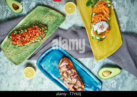 Bruscheta mit verschiedenen Füllungen auf Blau, Grün und Gelb. Schöne Gerichte. Hellgrau hinterlegt. Restaurant Menü Stockfoto