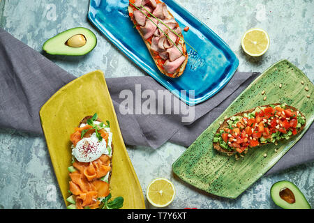 Bruscheta mit verschiedenen Füllungen auf Blau, Grün und Gelb. Schöne Gerichte. Hellgrau hinterlegt. Restaurant Menü Stockfoto