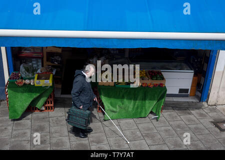 Eine ungesehen Mann Spaziergänge mit der Adjutant von einem weissen Stock vorbei an einem lokalen Obst und Gemüse shop, am 8. Mai 2019 in London, England. Stockfoto