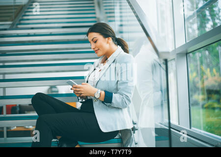 Hübsche junge business Frau sitzt auf der Treppe am Büro- und Mobiltelefon verwenden Stockfoto