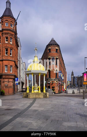 Der gusseiserne 1870er-Trinkbrunnen am Victoria Square Belfast erinnert an das Leben von Daniel Jaffe mit der flatiron Shape Bittles Bar im Hintergrund Stockfoto