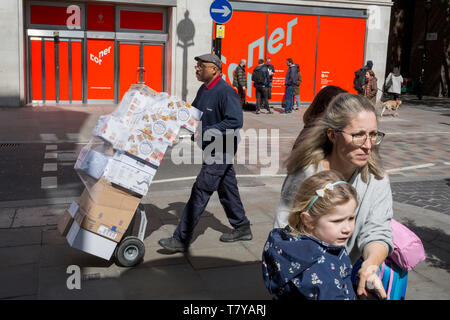 Ein Delivery Man schiebt einen Trolley von Boxen Vergangenheit eine Dame und Kind auf Long Acre in der Nähe von Covent Garden, am 9. Mai 2019 in London, England. Stockfoto