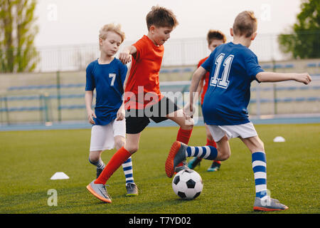 Junge Fußball-Spieler kicken Kugel auf dem Fußballfeld. Fußball horizontale Hintergrund. Jugend Junior Sportler in roten und blauen Trikots Stockfoto