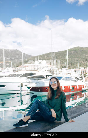 Eine schöne, junge Mädchen in der Sonnenbrille sitzt neben Yachten in Porto Montenegro Kotor in Montenegro. Stockfoto