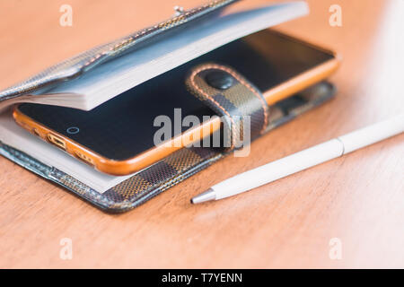 Ein gelbes Telefon liegt in einem Leder notepad auf einem Holztisch. Stockfoto