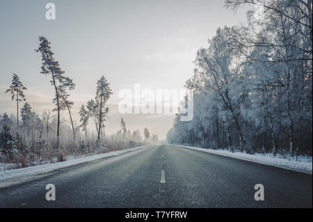 Blick auf die Autobahn Straße im Winter. Reisen Hintergrund. Gerade asphaltierte Landstraße, durch den Wald. Lettland. Ostsee. Stockfoto