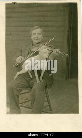 Mann spielt Violine mit einem Hund auf seinem Schoß, 1909. Rpc Stockfoto