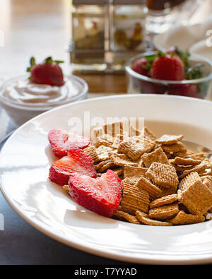 Eine Schüssel Müsli mit Erdbeeren als Teil einer ausgewogenen Frühstück. Joghurt, Eier, Erdbeeren und unscharf im Hintergrund. Stockfoto