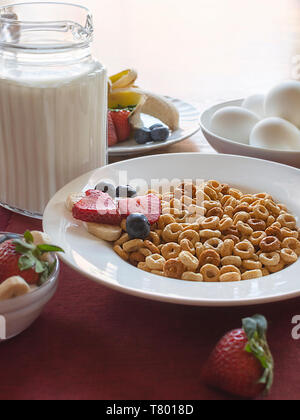 Eine Schüssel Müsli mit Obst, Milch und Eier, als Teil eines ausgewogenen Frühstück. Schüssel auf einem roten Unterlage mit Holztisch verschwommen im Hinterg Stockfoto