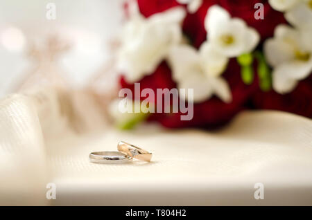 Schöne Hochzeit Ringe auf einem weißen Hintergrund mit einem weißen und roten Bouquet Stockfoto