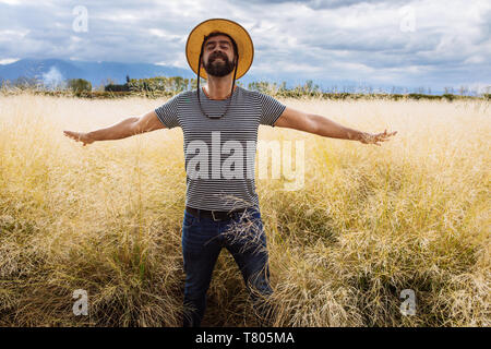 Mann in den späten dreißiger Jahren Mitte vierzig, posiert mit offenen Armen und Augen in einem gelben Gras Feld in Bodega Septima Weingut in Mendoza, Argentinien geschlossen. Stockfoto