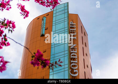 Sibiu, Rumänien - 22. April 2019: Golden Tulip Ana Tower Hotel mit seiner Panoramasicht auf den Aufzug, als von der Straße aus gesehen, von rosa Baum Blumen eingerahmt. Stockfoto