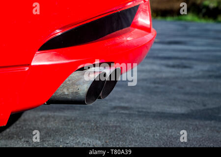 Auspuffrohre aus einem leuchtend roten Sportwagen mit einem V8-Motor. Im Gegensatz zu den schwarzen Asphalt und Gras im Hintergrund. Stockfoto