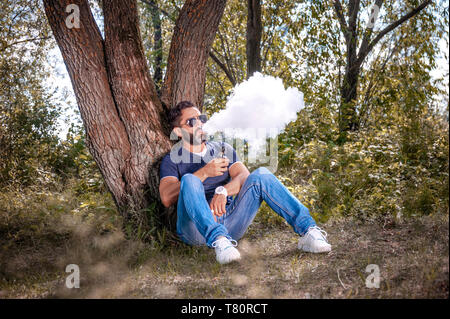 Stilvolle brutale vape Mann genießen die e-Zigarette in den Wäldern. Schöner Mann. Stockfoto