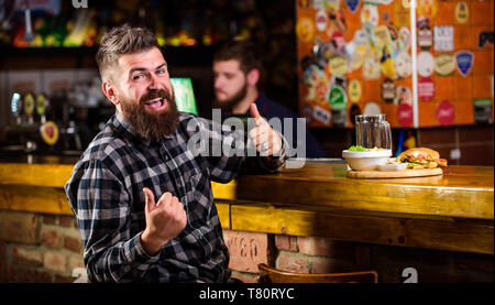 Essen im Pub. Kalorienreiche Snacks. Hipster entspannen im Pub. Pub ist ein entspannender Ort Drink zu entspannen. Brutale hipster bärtigen Mann an der Theke sitzen. Mann mit Bart Bier trinken essen burger Menü. Stockfoto