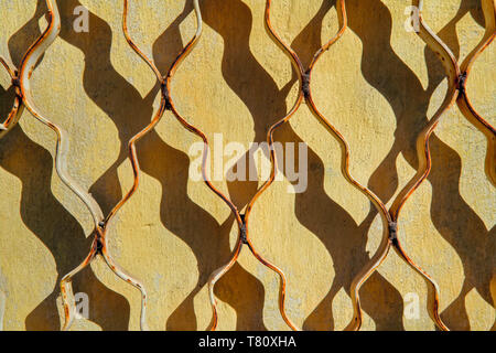 Die Textur einer gelben alten Verputzte Wand mit Rissen bedeckt und geschlossenes Metallgitter. Stockfoto