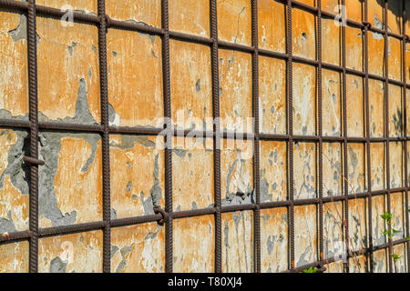Die Textur einer gelben alten Verputzte Wand mit Rissen bedeckt und geschlossenes Metallgitter. Stockfoto