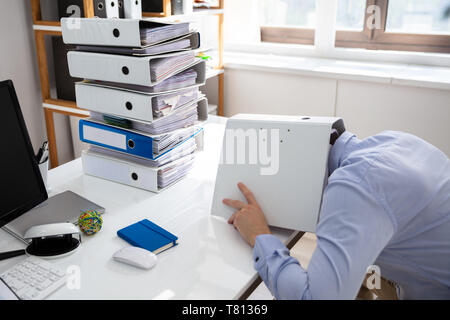 Betonte Geschäftsmann versteckt unter Ordner während der Arbeit am Schreibtisch Stockfoto
