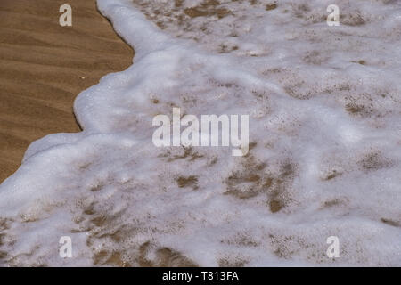 Meer oder ozeanische Welle waschen über Sand - schaumiges Muster, Hintergrund. Foto von nassem Sand am Strand. Stockfoto