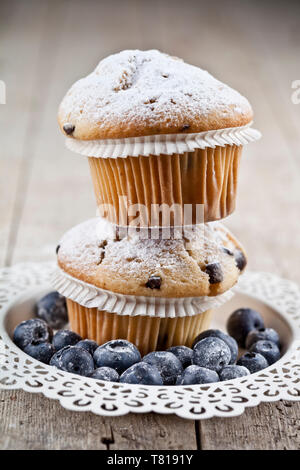 Zwei hausgemachte frische Muffins mit Zucker Pulver und Heidelbeeren auf weiße Platte auf rustikalen Holztisch Hintergrund. Stockfoto