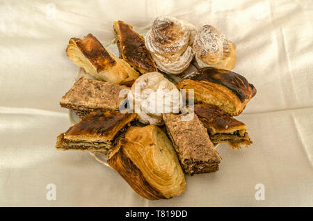 Porzellanteller mit Scheiben von verschiedenen Kuchen und eclairs mit traditionellen armenischen 'gata' Cookies aus Blätterteig auf einer weißen Tischdecke Stockfoto