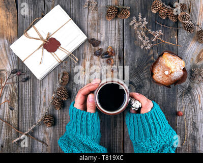 Frauen Hände halten eine Keramik Becher mit Kaffee schwarz, grau Holztisch, in der Nähe von einem Stapel Papier Karten, Ansicht von oben Stockfoto