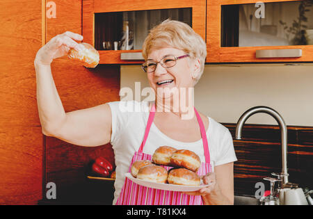 Lächelnde ältere Frau ihre hausgemachten Krapfen in der Küche. Stockfoto