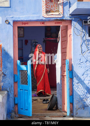 Sambhar, Indien - Februar 03, 2019: Indische Frau in Rot Sari in der Tür des Blauen Haus in Sambhar Lake Village. Rajasthan Stockfoto