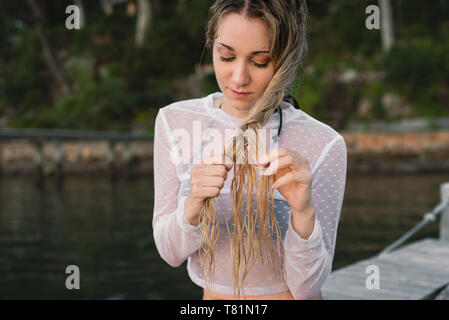 Frau sitzt auf einem Steg, ihre langen Haare flechten nach dem Schwimmen. Stockfoto