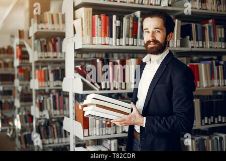 Mann, der in einer Bibliothek. Kerl in einem schwarzen Anzug. Studenten mit einem Bücher. Stockfoto
