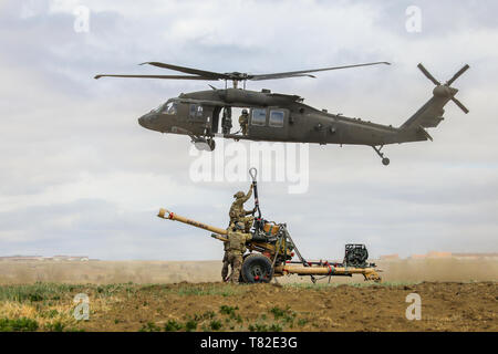 Ein UH-60 Black Hawk, die von Mitgliedern des 4 Combat Aviation Brigade pilotiert, 4 Infanterie Division, schwebt in der Nähe von eine M119 Haubitze und Soldaten aus Bravo. Akku, 2. Battalion, 77th Field Artillery Regiment, 2 Infantry Brigade Combat Team, 4. Inf. Div., 2. Mai 2019, während der Angriff auf Fort Carson, Colorado. (U.S. Armee Foto: Staff Sgt. Neysa Canfield) Stockfoto