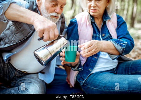 Senior Paar gießen Kaffee bei einem Picknick auf dem Campingplatz im Wald Stockfoto